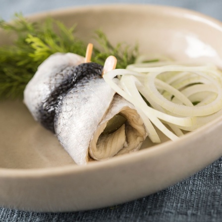 Ein Rollmops mit Zwiebeln auf einem Teller. 