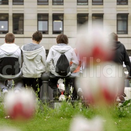 Jugendliche sitzen auf einem Zaun an der Straße.