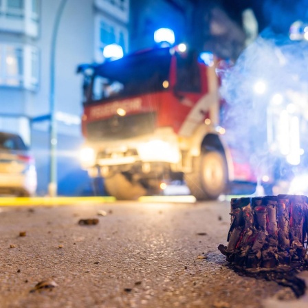 Abgebrannte Böller liegen auf einer Straße in Berlin, im Hintergrund steht ein Feuerwehrauto.