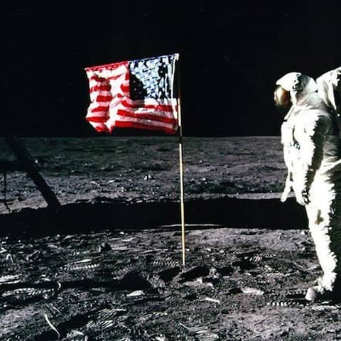 Astronaut steht auf dem Mond vor einer Flagge