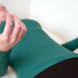 Eine Frau übt im Liegen progressive Muskelrelaxation aus.