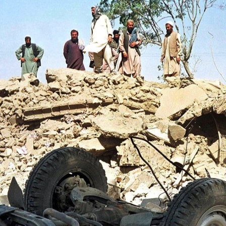 Afghanen blicken am 9.10.2001 auf die Trümmer des Gebäudes der von den Vereinten Nationen (UN) finanzierten Minenräumorganisation Afghan Technical Consultants in Kabul. Vier afghanische Mitarbeiter wurden durch den Einschlag einer Cruise Missile getötet.