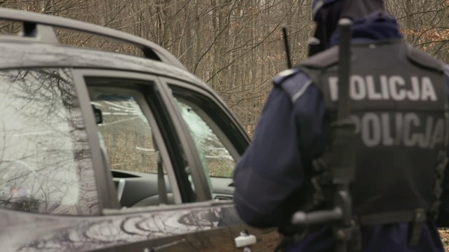Ein polnischer Polizist vor einem Auto mit eingeschlagenen Scheiben.