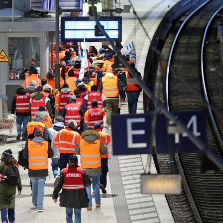 Streikende Mitglieder der EVG tragen Fahnen und Streikwesten und gehen über einen Bahnsteig im Hamburger Hauptbahnhof.
