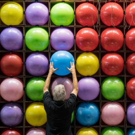 Zur Dekoration eines Standes bringt ein Messebauer zahlreiche bunte Luftballons an eine Wand an.