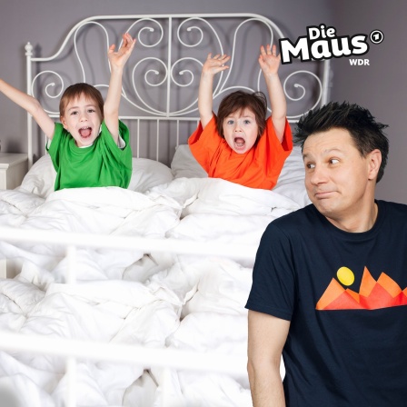 Moderator André schaut lachend auf zwei Kinder, d im Bett sitzen und die A