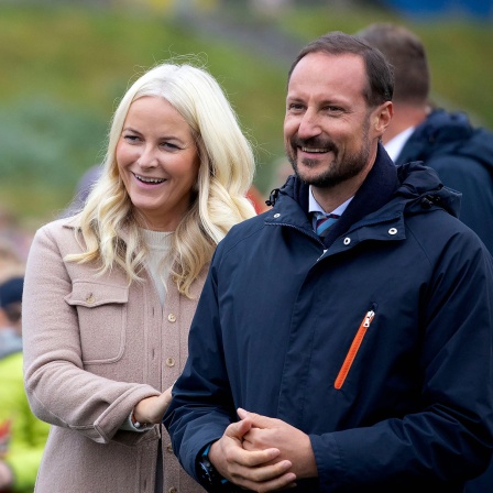Kronprinz Haakon und Kronprinzessin Mette-Marit - das Royale Traumpaar zum Anfassen im Podcast &#034;Annelies Royale Welt&#034;. Auf dem Bild steht das Paar eng beieinander und lächelt. Sie trägt eine helle Jacke, er eine dunkelblaue Jacke mit Kapuze.