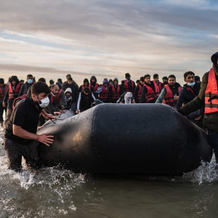 Migranten ziehen ein Schlauchboot aus dem Wasser am Strand von Gravelines.
