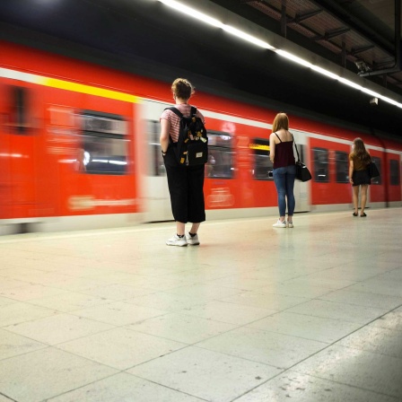Reisende mit Mundschutzmaske, warten auf einfahrende S-Bahn