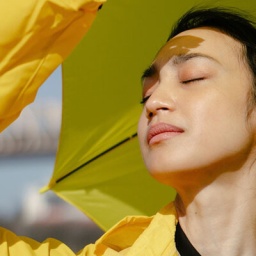 Frau in gelbem Regenmantel genießt die Sonnenstrahlen auf ihrem Gesicht