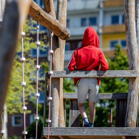 Ein Kind steht auf einem Spielplatz vor einem Plattenbau.