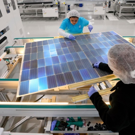 Zwei Frauen arbeiten in einer Fabrik an Solarpaneelen. 