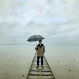 Bjarne Mädel als Kriminalkommissar Sörensen auf einem Steg im Wasser, einen Regenschirm über sich haltend.