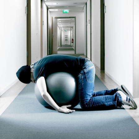 Ein Mann liegt in einem Büroflur auf einem Gymnastikball.