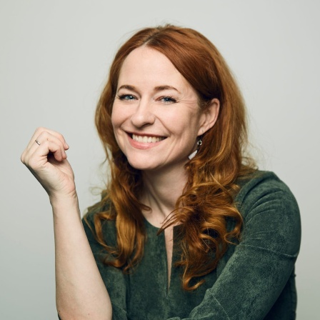 Moderatorin Katrin Schumacher sitzt vor einem Bücherregal zwischen Büchern