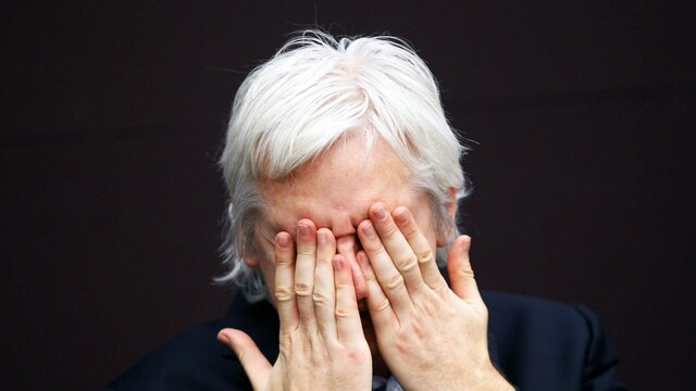 Julian Assange nah, hält sich die Hände vor seine Augen