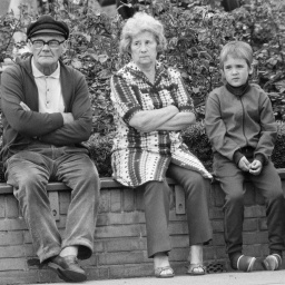 Opa, Oma und ihr Enkel sitzen nebeneinander auf einer Mauer