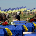 Angehörige und Freunde nehmen an der Begräbnisfeier für 13 an der Front gefallenen ukrainische Soldaten teil. Die Särge sind in einer Reihe aufgestellt und jeweils mit einer ukrainischen Fahne abgedeckt.