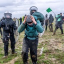 Zwei Polizisten in Schutzkleidung verfolgen einen Demonstranten auf einem Feld bei Lützerath