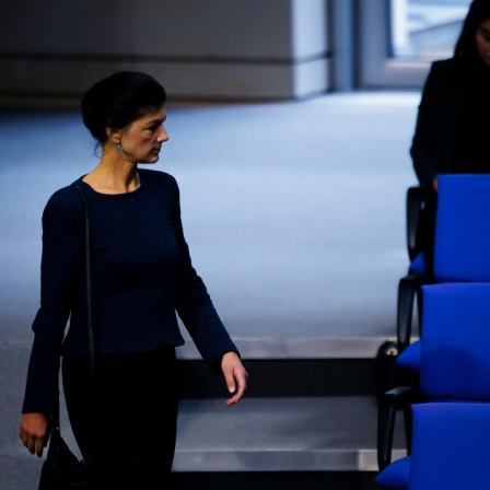 Sahra Wagenknecht geht im Plenarsaal des Deutschen Bundestags an den blauen Stuhlreihen vorbei.