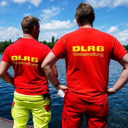 Zwei Menschen mit DLRG-Shirt stehen an einem See (2021).