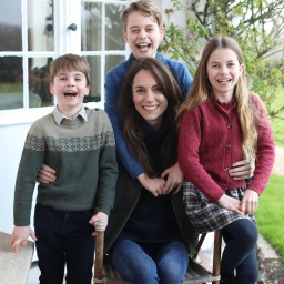 Familienfoto, auf dem Catherine, Princess of Wales, lächelnd auf einem Stuhl sitzt und von ihren drei Kindern umringt wird.