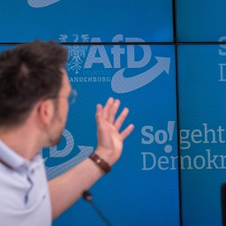 Dennis Hohloch, Parlamentarischer Geschäftsführer der AfD-Fraktion im Landtag von Brandenburg, deutet während einer Pressekonferenz auf den Slogan "So! geht Demokratie".
