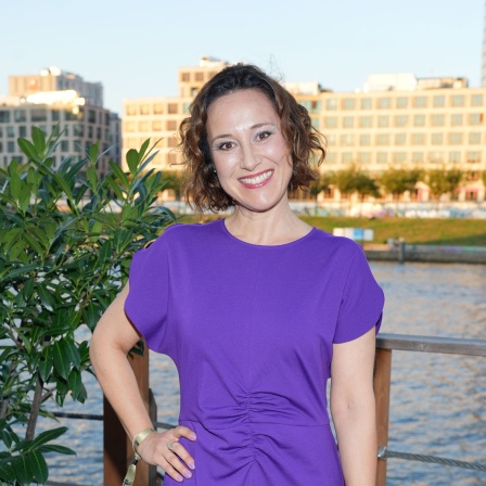 Bärbel Stolz steht vor einem Busch in einem lila Kleid