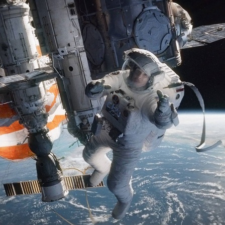 Ein Filmstill aus &#034;Gravity&#034; (2013): Sandra Bullock als Dr. Stone schwebt in einem Raumanzug im Weltall, hinter ihr sieht man weit entfernt die Erde