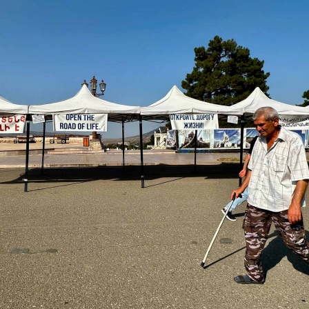 Ein Mann geht über einen leeren Platz an einem Pavillon vorbei, an dem ein Plakat mit der Aufschrift "Open the Road of Life" hängt.