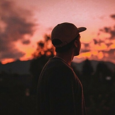 Eine Person mit Kappe steht vor einem Sonnenuntergang