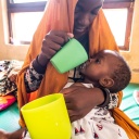 Eine Frau füttert ein Baby mit einem Becher.