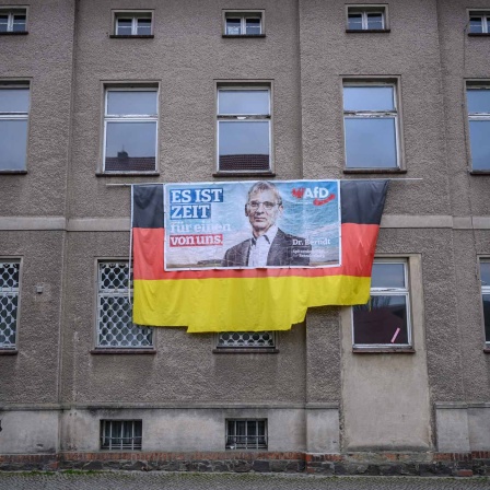 Ein Wahlplakat von Hans-Christoph Berndt, Vorsitzender der Brandenburger AfD-Fraktion, hängt auf einer Deutschlandflagge an einer tristen Hausfassade.