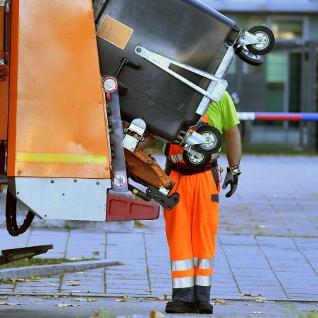 Ein Mitarbeiter der Müllentsorgung steht hinter einem Müllauto.