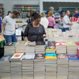 Besucher streifen um Stände mit Bücherstapeln herum.