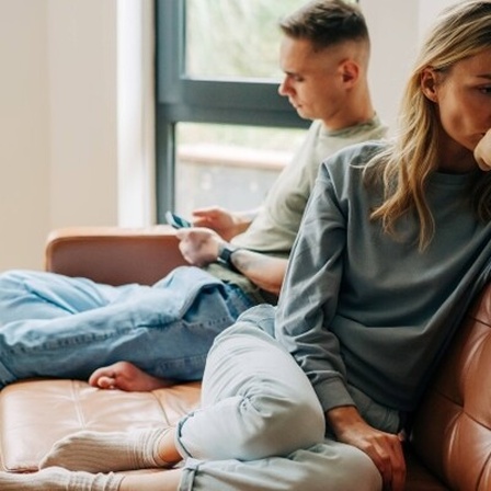 Ein Mann und eine Frau sitzen auf eine Couch. Sie hat ihm den Rücken zugewendet.