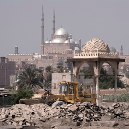 Ein Bulldozer rangiert inmitten von Trümmern vor dem Hintergrund einer Moschee.