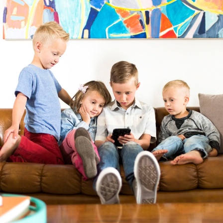 Vier Kinder sitzen auf einer Couch und schauen auf ein Smartphone (Bild: picture alliance / Bildagentur-online/Tetra Images)