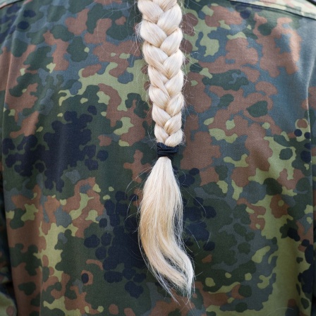 Rücken einer Person in Uniform mit blondem Zopf
