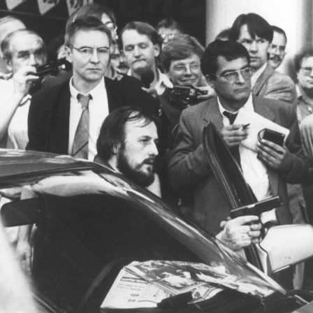 Mit einer Waffe in der Hand fordert der am Steuer des Fluchtfahrzeugs sitzende Hans-Jürgen Rösner am 18.08.1988 in der Innenstadt von Köln die umstehenden Journalisten und Passanten auf, den Weg frei zu machen.