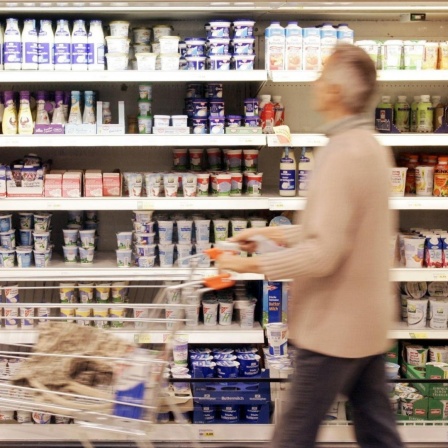 Ein Supermarktregal mit Plastikverpackungen. Davor geht ein grauhaariger Mann mit einem Einkaufswagen.