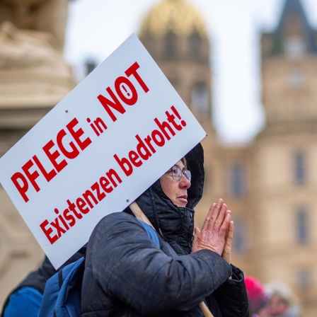 Bei einer Protestaktion hält eine Teilnehmerin ein Schild mit der Aufschrift "Pflege in Not - Existenzen bedroht!".