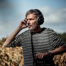 Kai Grehn, mit Kopfhörern und Tongerät, steht auf einem Feld