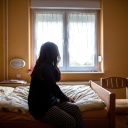 Eine Frau sitzt in einem Frauenhaus auf einem Bett © dpa/Maja Hitij