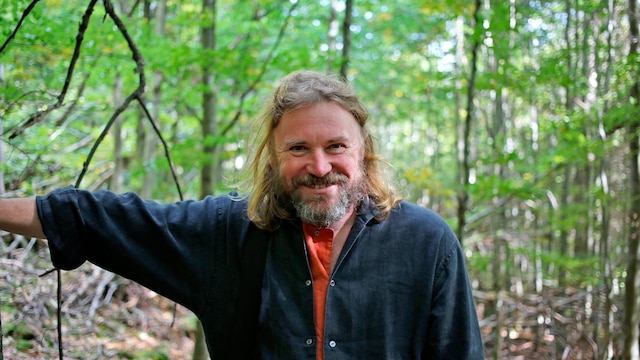 Männliche Person mit Bart lächelnd in einem Wald