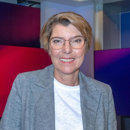 Bettina Böttinger mit wei2em T-Shirt und grauer Jacke im Studio bei Maischberger. Sie guckt in die Kamera.
