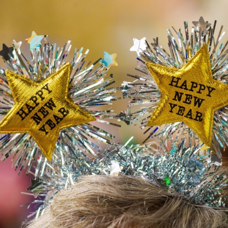 Ein Frau begrüßt das Neue Jahr mit einem Kopfschmuck mit der Aufschrift &#034;Happy New Year&#034;.