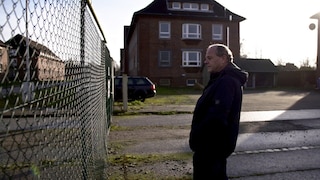 Anwohner Jürgen Fehrs blickt durch den Zaun auf die ehemalige Kaserne in Glückstadt, die eine Abschiebungshafteinrichtung werden soll.