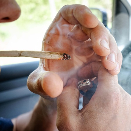 Symbolbild: Ein Mensch mit Joint am Steuer eines Autos.