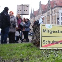 Bei der 8. Meile der Demokratie in Magdeburg stehen Personen auf einer Straße. Vor ihnen steht ein Schild, das einem Verkehrsschild nachgeahmt ist, darauf steht "Mitgestalten" verbunden mit einem Pfeil und Schulterzucken, das durchgestrichen ist (Januar 2016)